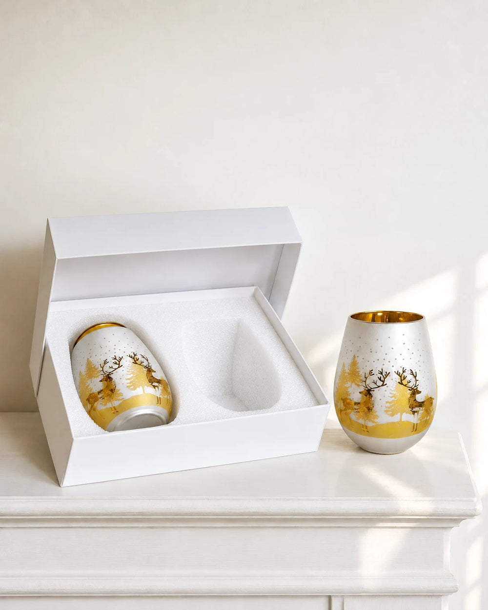White foam gift box with one complete gold and silver deer glass lying flat and a second glass standing beside it