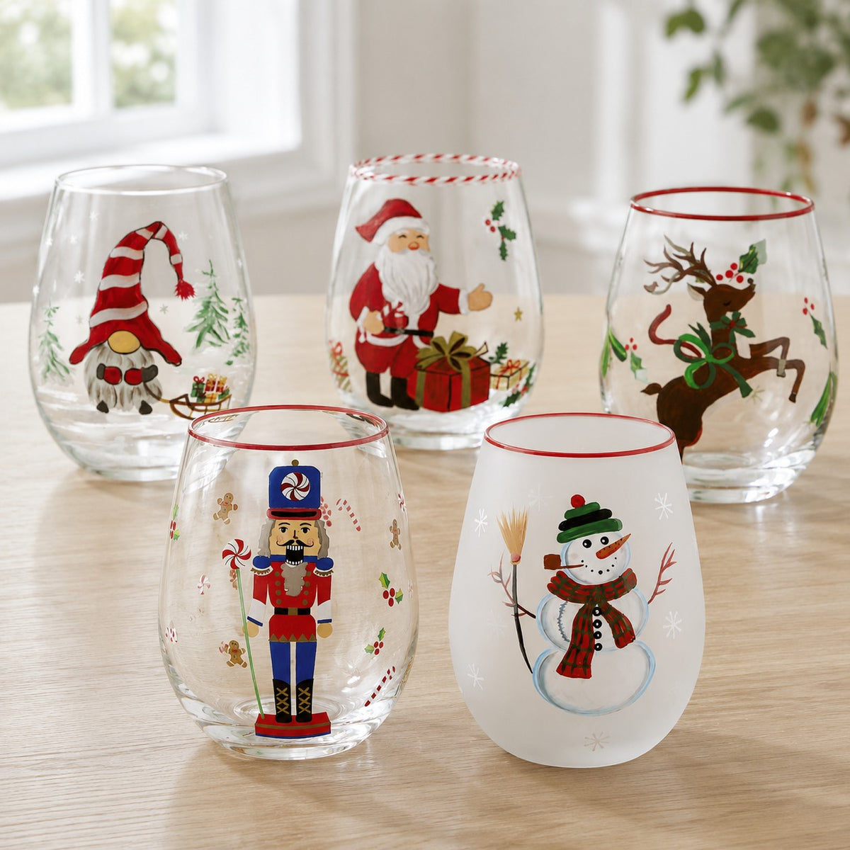 Hand-painted Christmas stemless wine glasses on a sunlit table - gnome, Santa, reindeer, nutcracker and frosted snowman designs