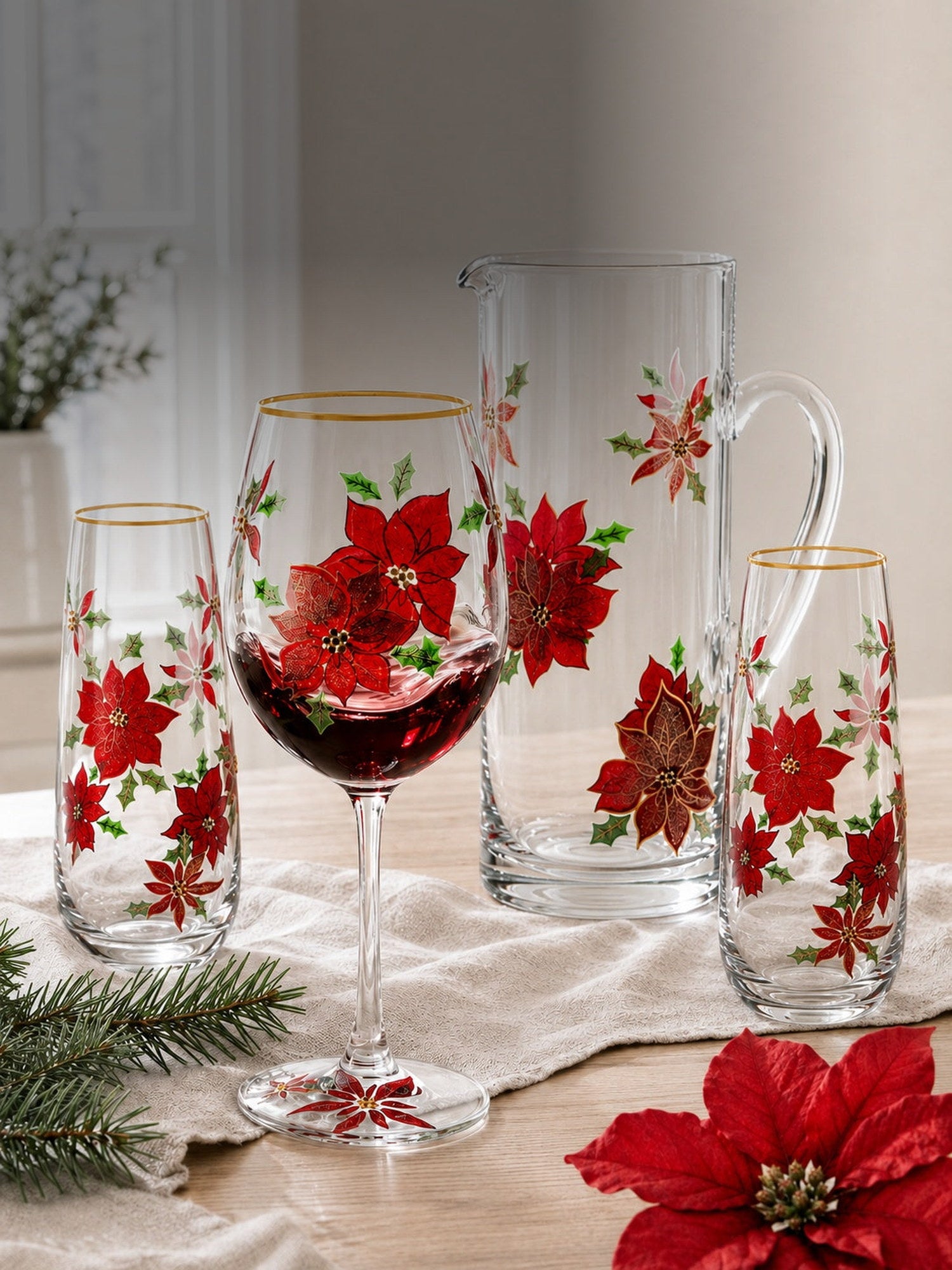 Hand-painted poinsettia wine glass, pitcher and stemless flutes on a sunlit table